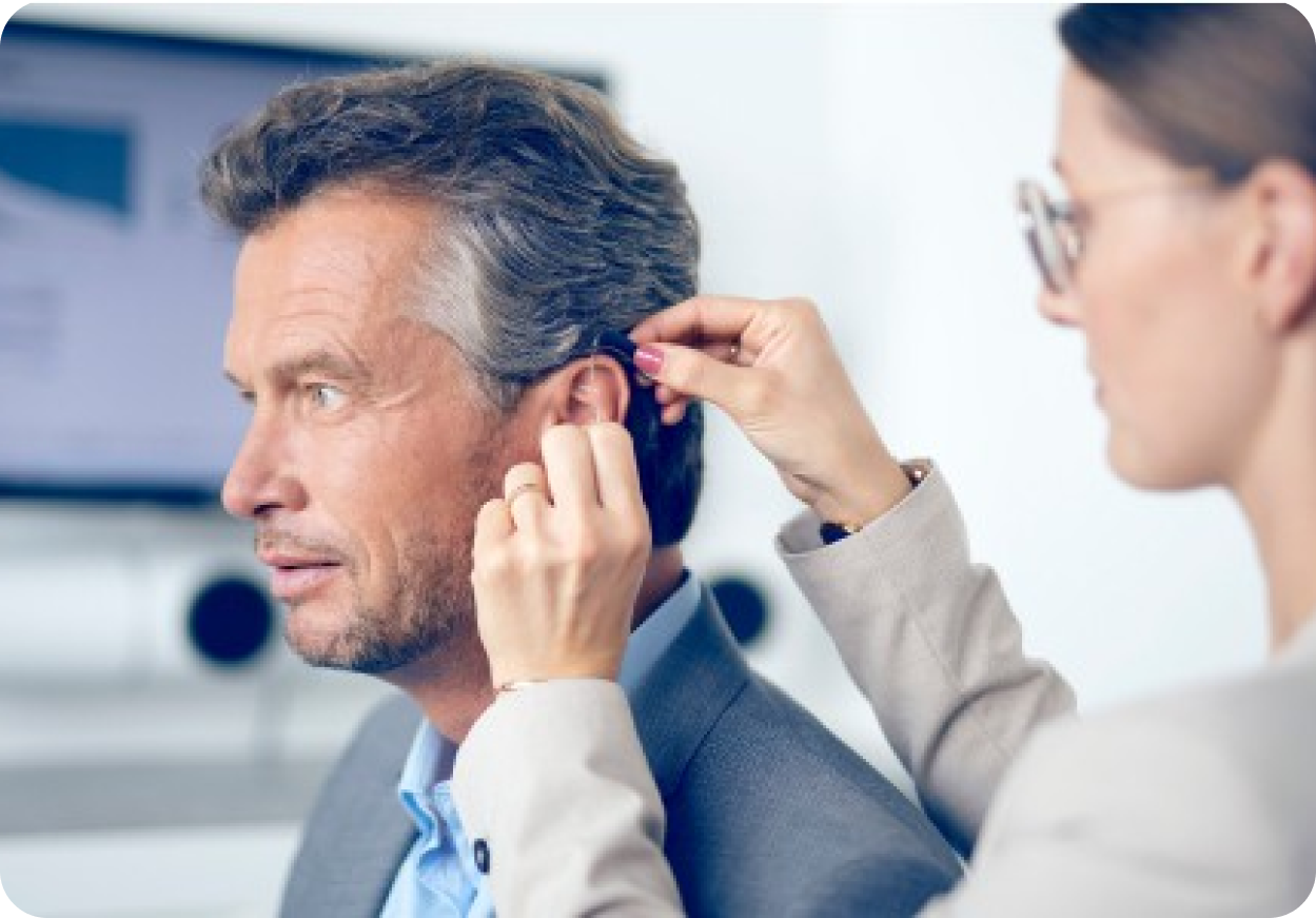 Vrouwelijke audicien doet achter-het-oor gehoorapparaat in bij man