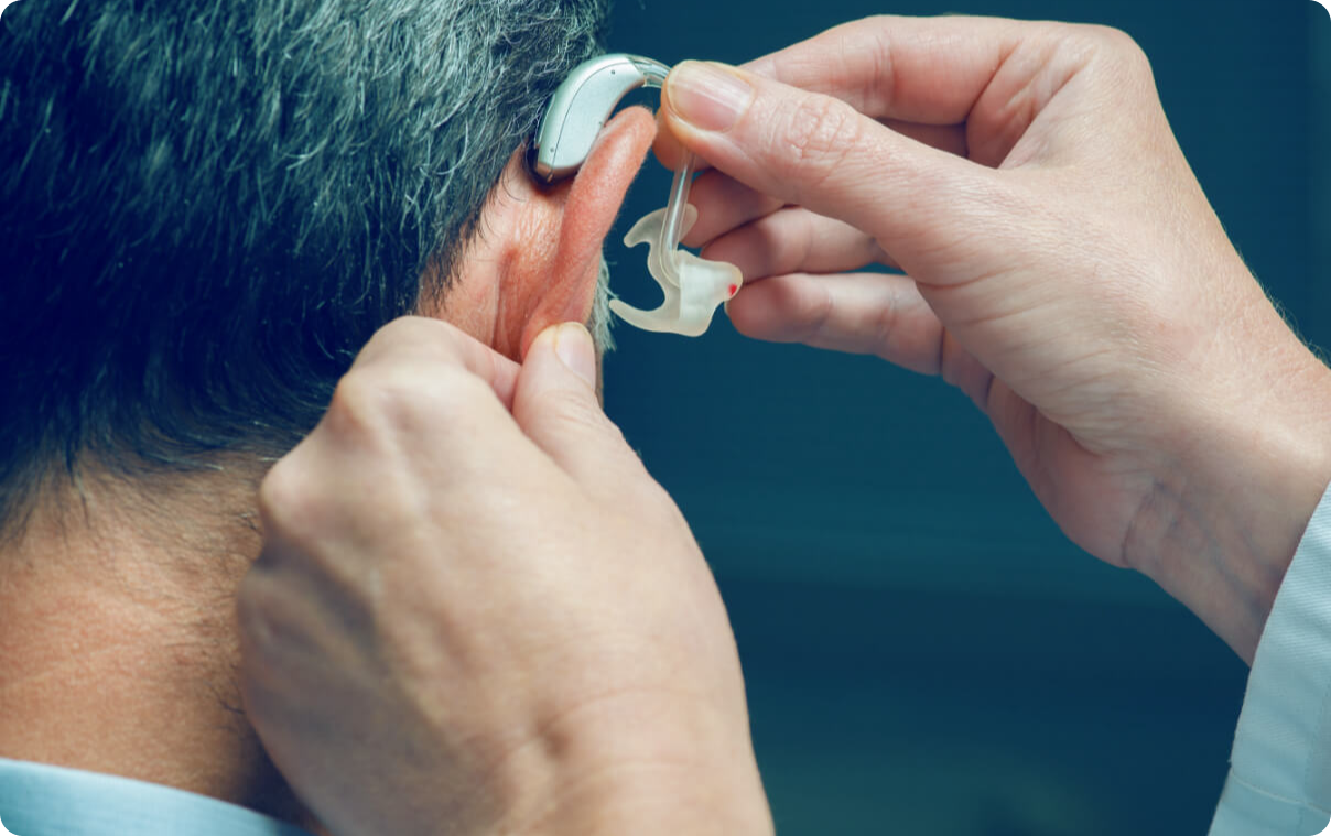 Iemand die achter-het-oor gehoorapparaat met oorstukje omdoet bij een man