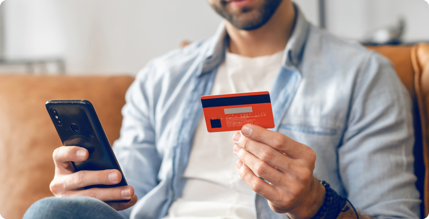 man op de bank met zijn smartphone en bankpas in de hand