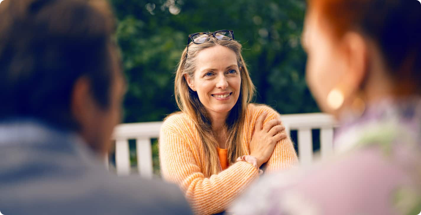 Lachende vrouw die in de tuin zit en aan het genieten is van een gesprek met vrienden