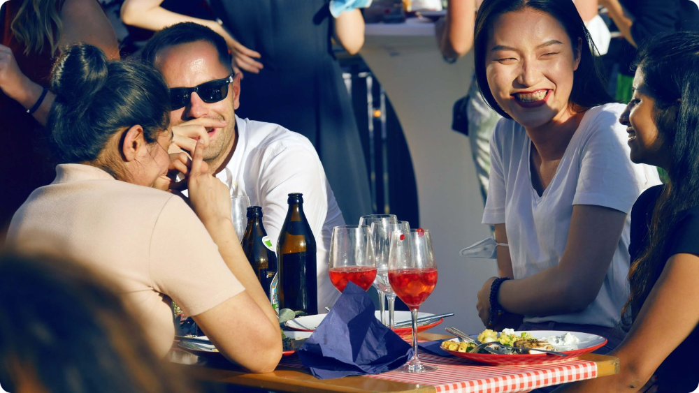twee mannen en twee vrouwen zitten aan een tafel in de zon met een drankje voor zich