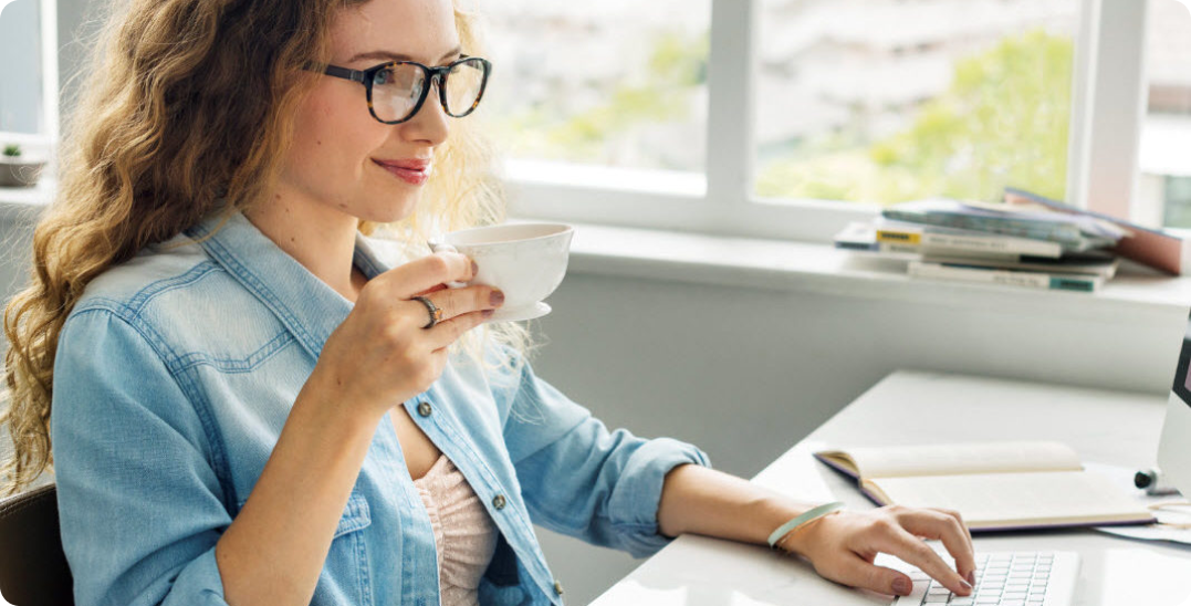 jonge vrouw zit achter haar computer met een kopje koffie in haar hand