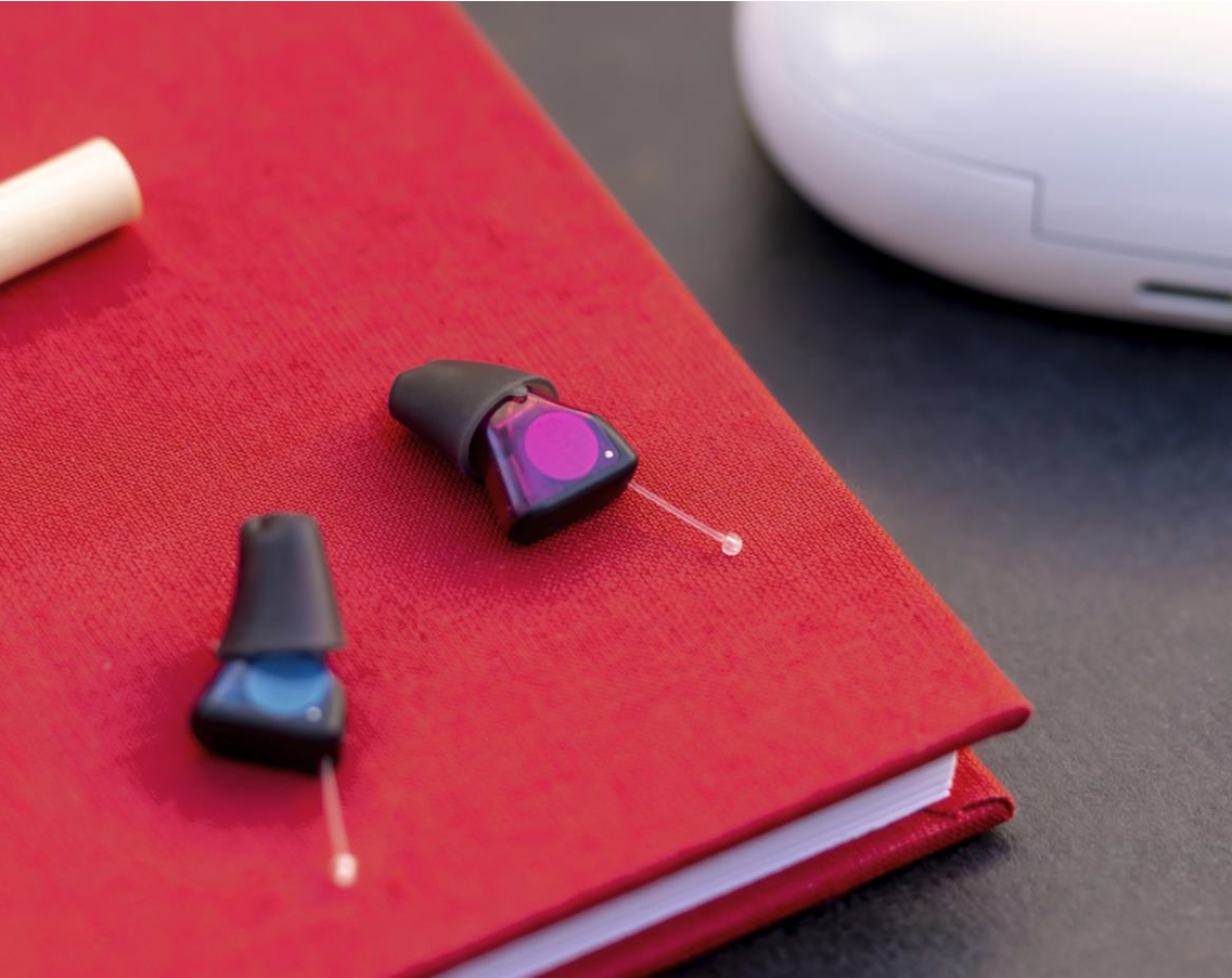 twee signia silk charge en go ix gehoorapparaten liggen op een rood schrift op tafel met de oplader ernaast
