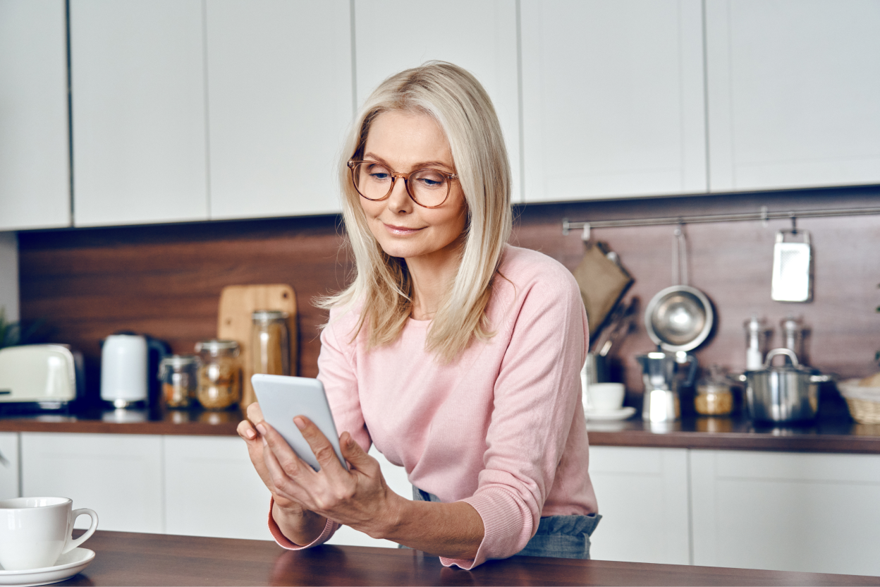 een vrouw staat in de keuken en kijkt op haar mobiel